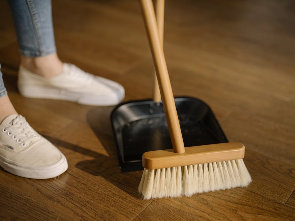 Person Wearing White Pants and White Socks Standing Beside Brown Broom